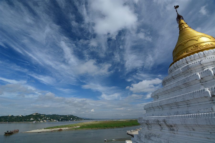 White stupa with a golden spire above a broad river in Myanmar